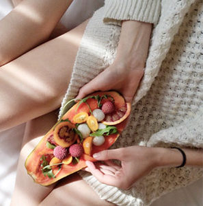 A woman sitting on a bed holding a plate of fruit