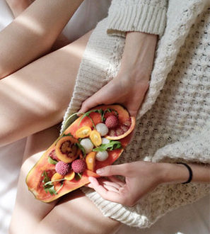 A woman sitting on a bed holding a plate of fruit