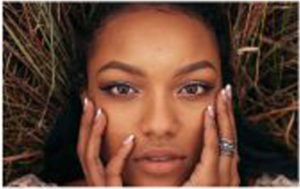 A woman is laying in the grass with her hands on her face.